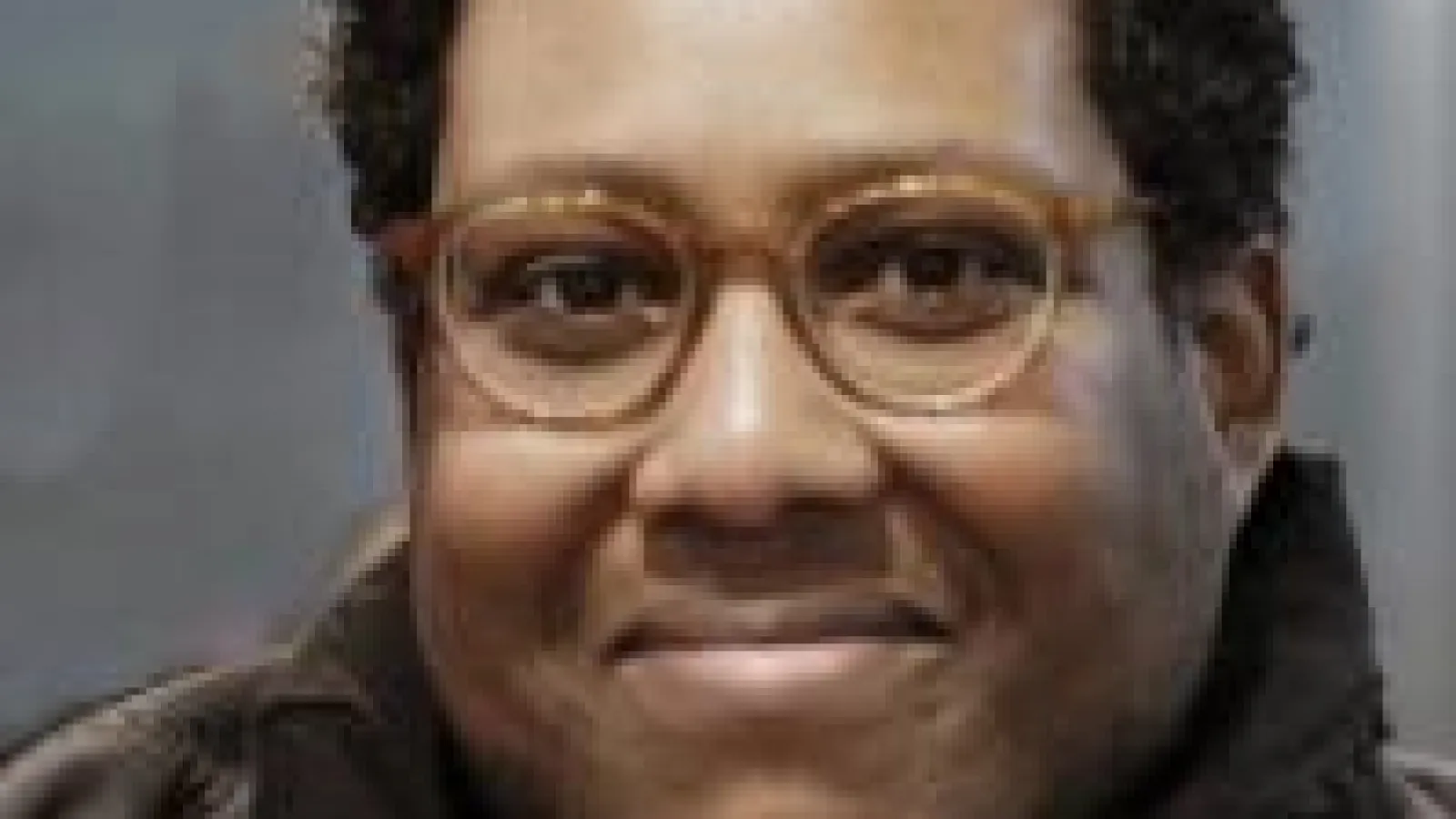 Qaman Omar smiling in front of grey background