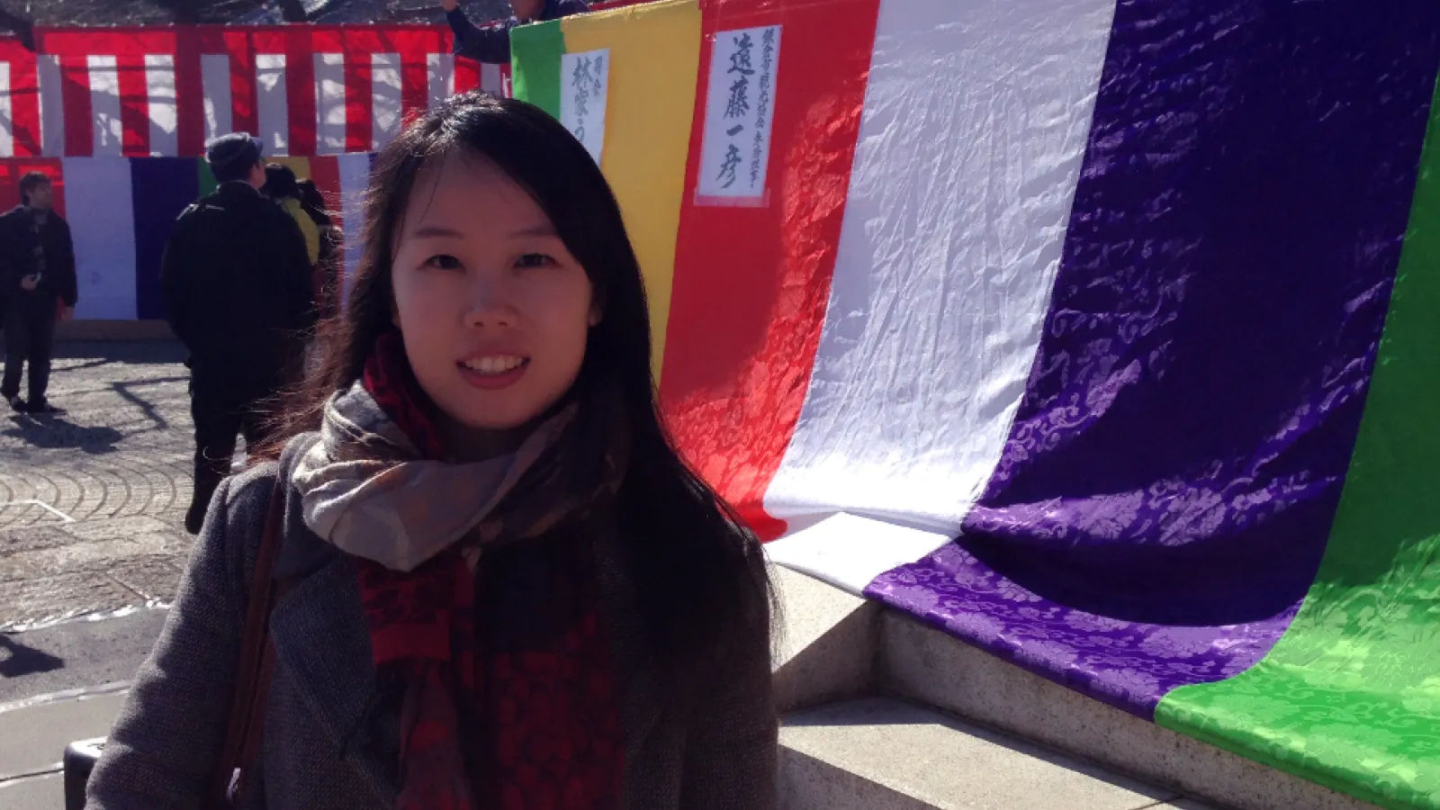 Yanfei Yin standing outside in front of colorful fabrics 